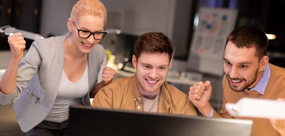 business team celebrating success at night office business, success and teamwork concept - happy coworkers with computer celebrating victory at night office