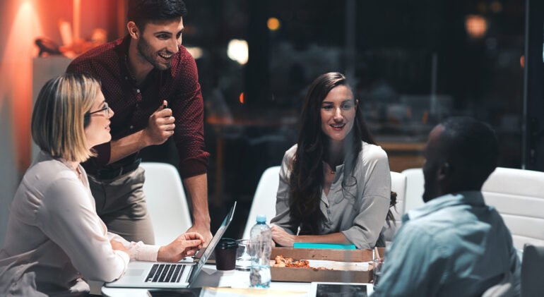 Business people, laptop and discussion for project at night in office, creative agency and overtime food for design. Teamwork, support and problem solving in pizza meeting for deadline and planning.